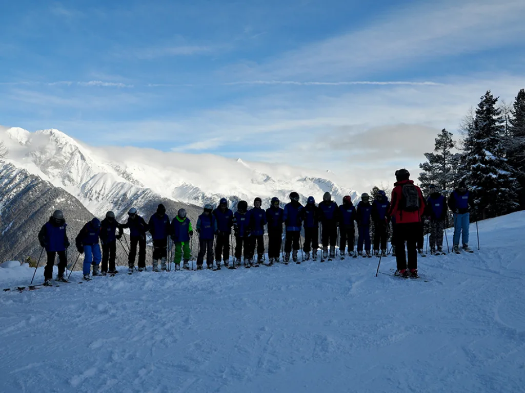 Lange Reihe von Skifahrenden vor dem verschneiten Bergpanorama.